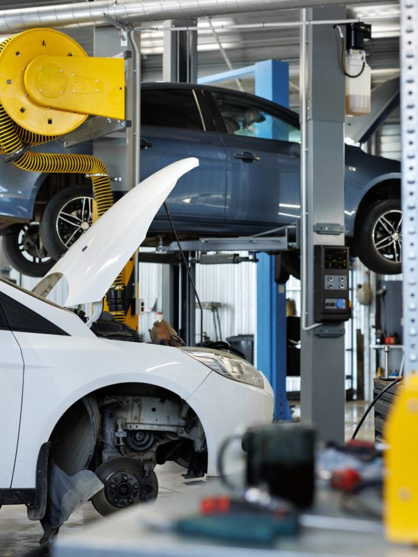 Zwei Autos werden in einer Autowerkstatt gewartet, eines davon mit offener Motorhaube.