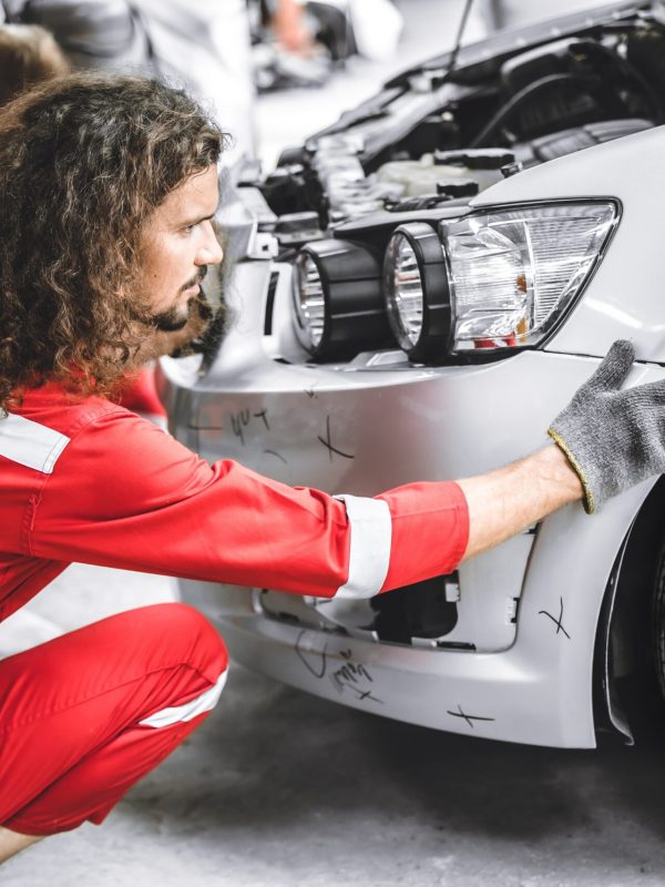 Mann in rotem Overall markiert den Kotflügel des Autos während der Karosserie-Unfallinstandsetzung.